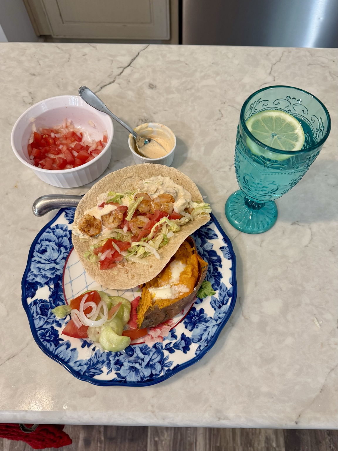 Shrimp tacos, sweet potato, and salad on a floral plate with lemon water